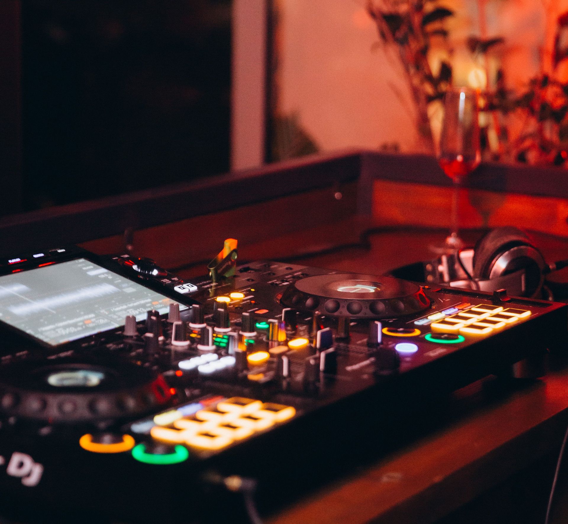 Colorful DJ mixer and headphones on a wooden table in a dimly lit nightclub, exuding a lively atmosphere.