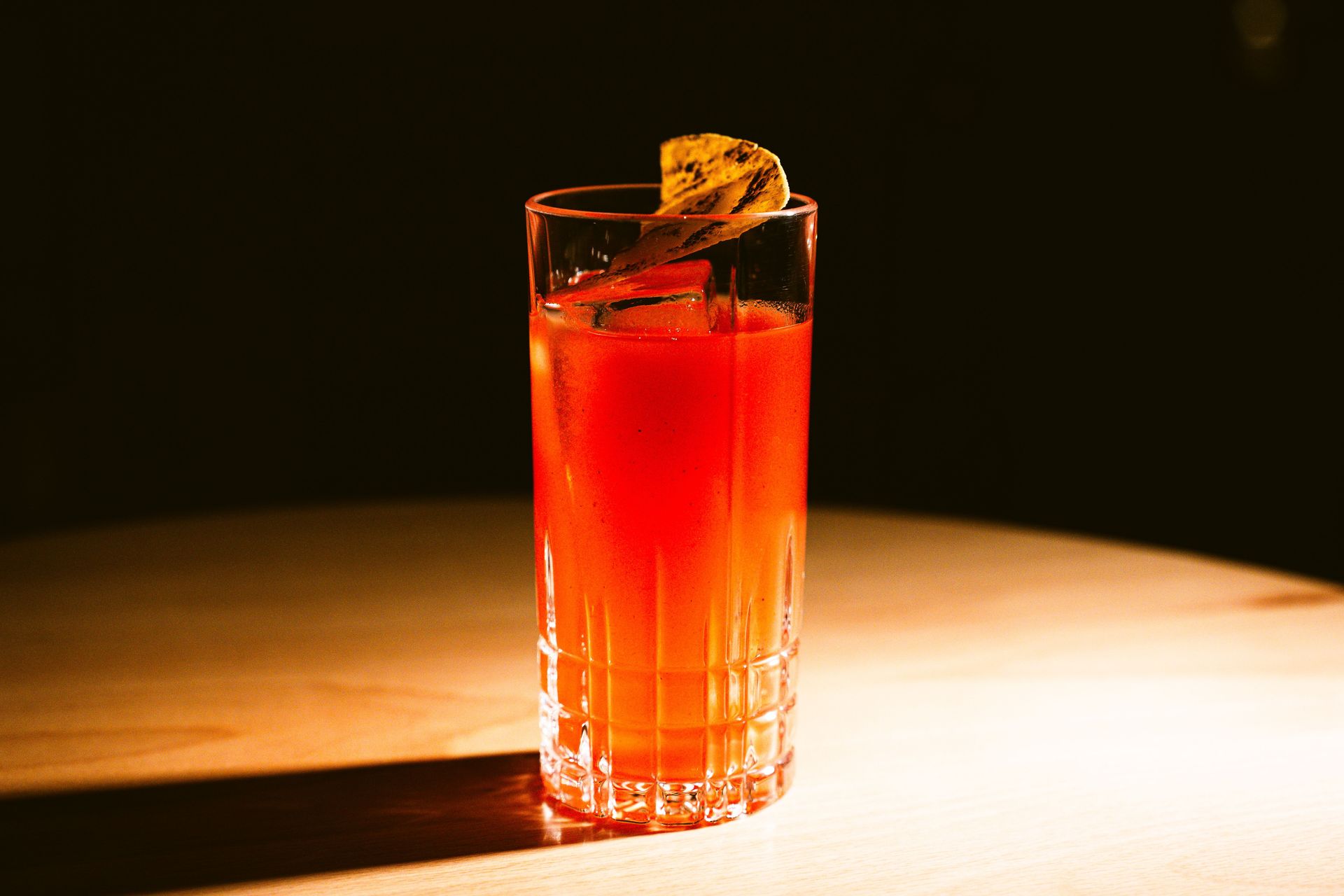A vibrant cocktail with a citrus garnish on a wooden table, beautifully lit to highlight its vivid color.